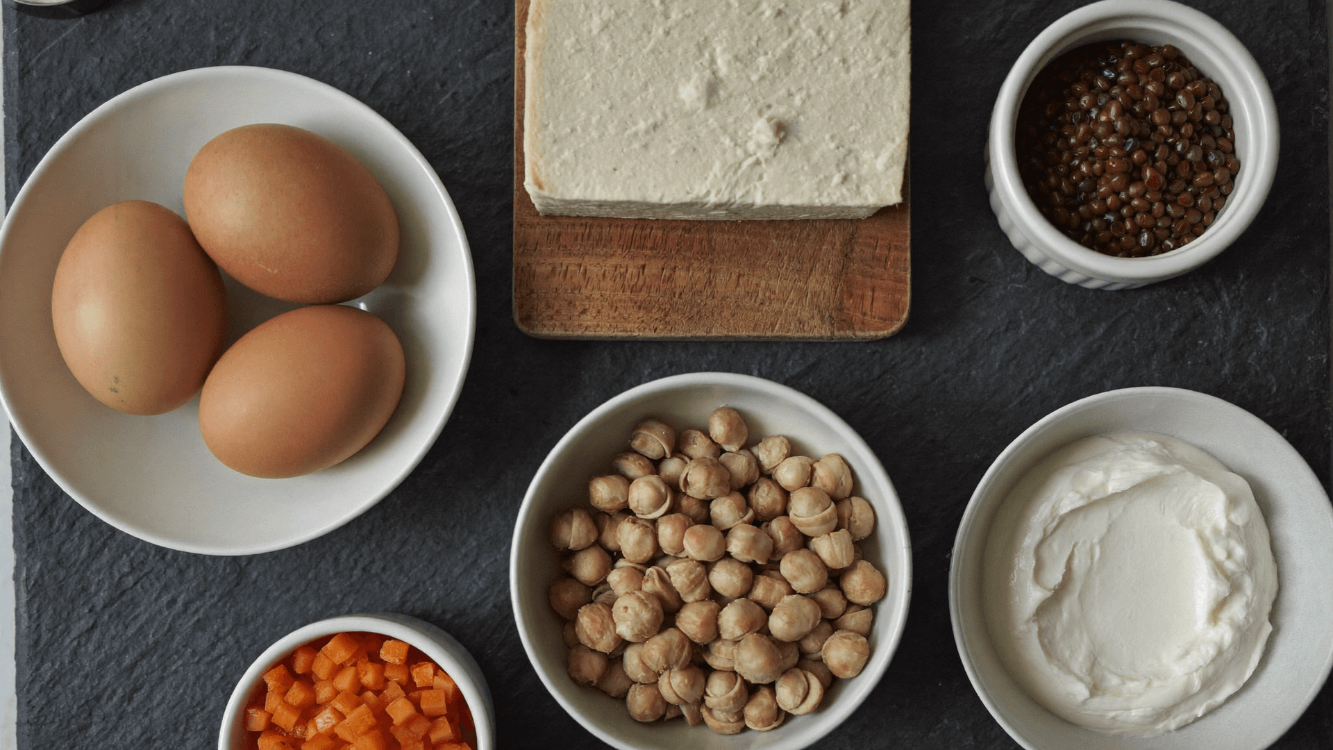Magerquark, getrocknete Linsen, Tofu, Thonkonserve und Pouletbrust nebeneinander auf einer Schweizer Küchenablage, daneben ein Notizzettel mit der Rechnung Franken pro 20 Gramm Protein